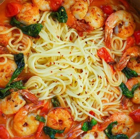Plate of shrimp pasta with garlic basil tomato sauce garnished with fresh herbs