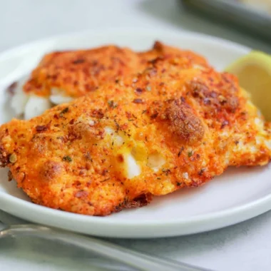 Baked Parmesan Crusted Cod fillets on a white plate with herbs